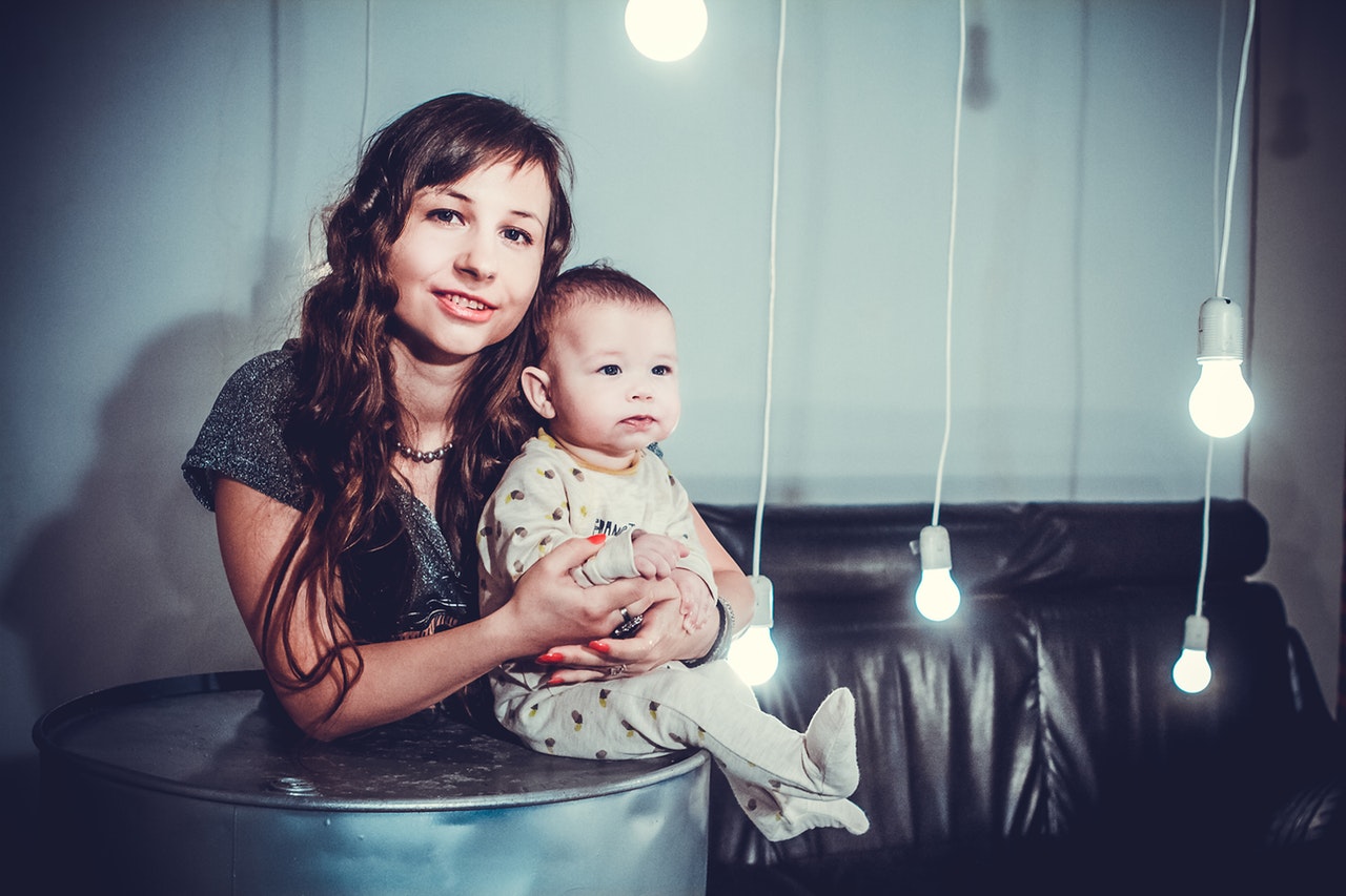 woman carrying baby beside white-led-light-bulbs