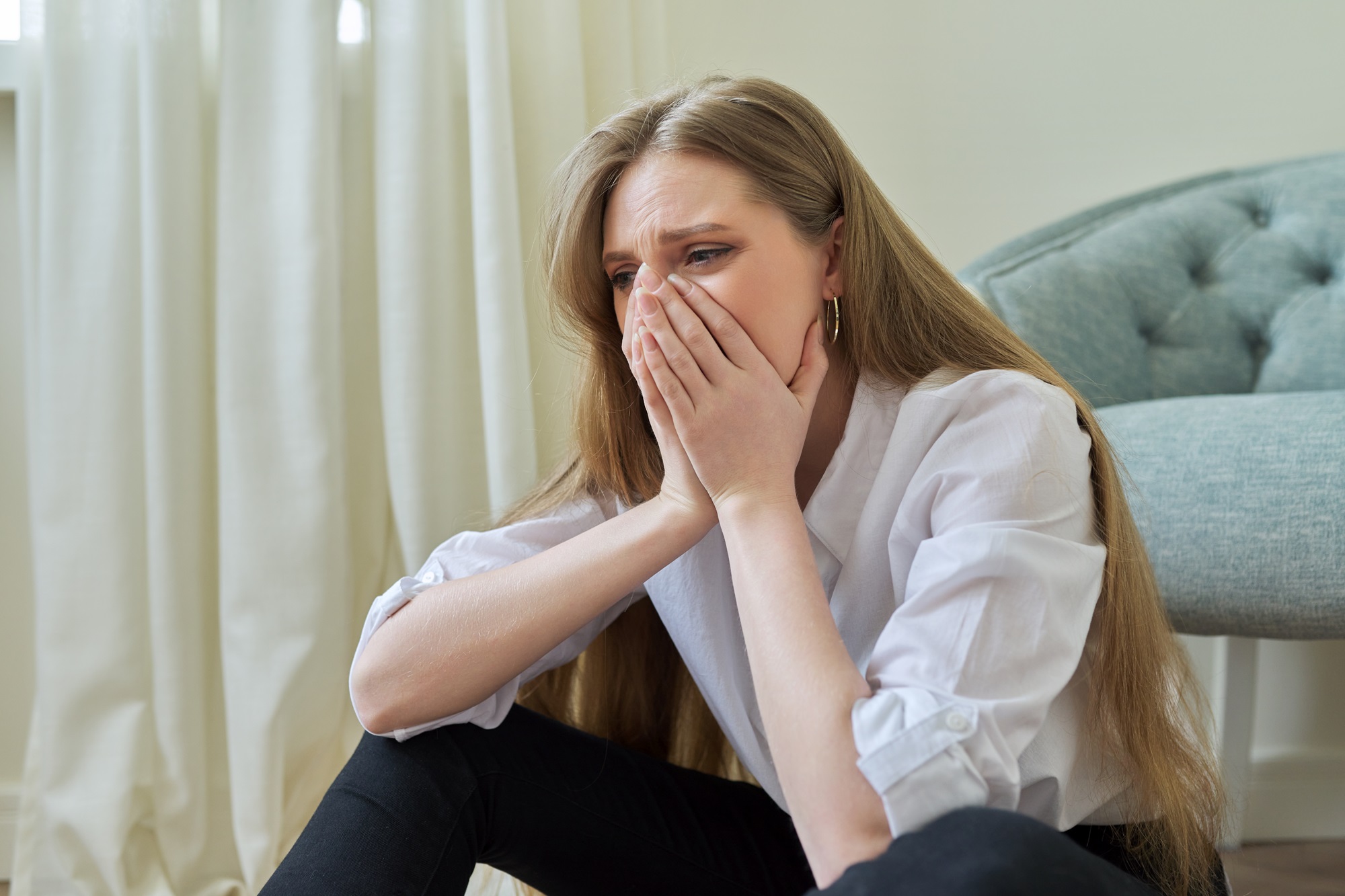 Upset crying young woman sitting at home
