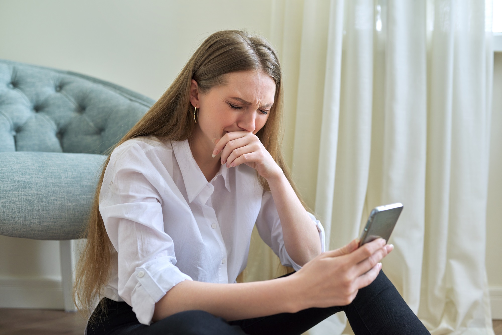 young woman crying while watching family videos on smartphone